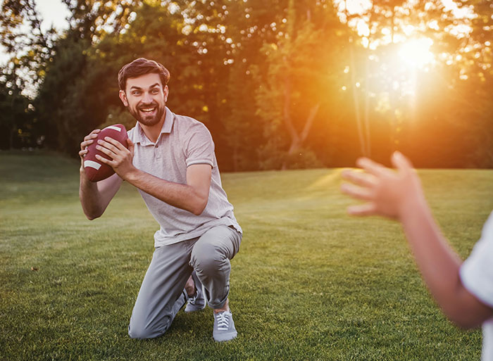 Young man playing football in a park, smiling brightly, embodying high school nostalgia on a sunny day.