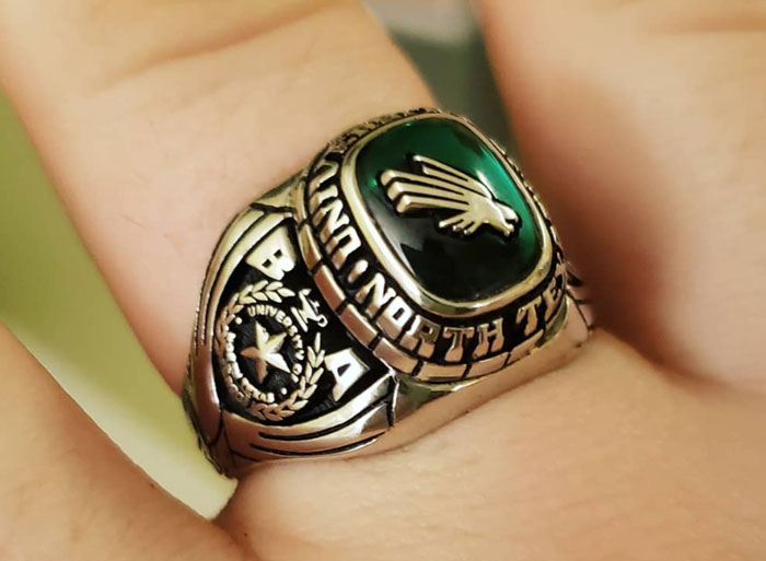 High school class ring with a green stone and intricate engravings worn on a finger.