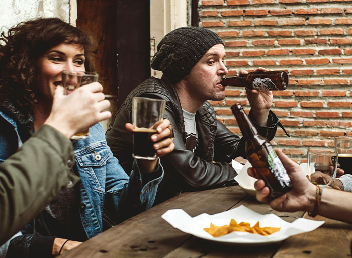 People enjoying drinks at a bar, embodying behaviors of peaking in high school, with beer bottles and glasses.