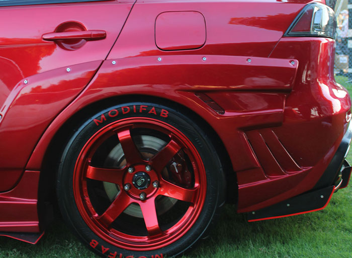 Customized red car with glossy finish and sporty wheels on grass, evoking high school nostalgia.