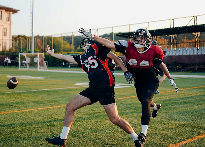 Two high school football players in action, one blocking a pass on the field.