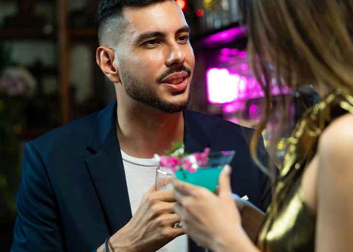 Man at a bar engaging in conversation, holding a drink; behavior reminiscent of having peaked in high school.