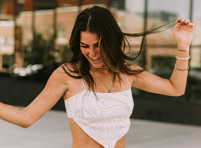 A woman joyfully holding her hair in a playful pose, embodying high school nostalgia vibes.