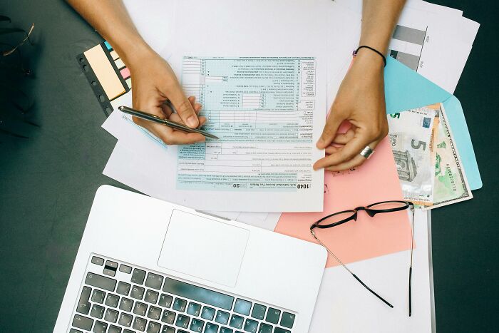 Hands filling out forms on a cluttered desk with a laptop, illustrating concepts people can't grasp easily.