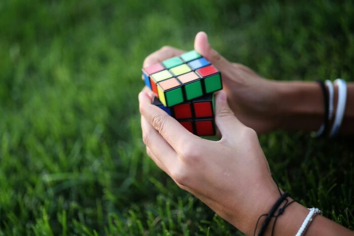 Hands holding a Rubik's Cube on grass, symbolizing things people struggle to grasp.