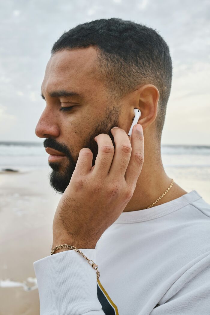 Man with short hair on beach, listening to music on earphones, pondering things he can't grasp, wearing a white sweater.