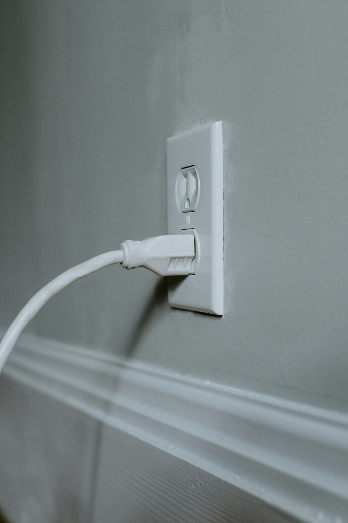 White plug inserted into an electrical outlet on a green wall.