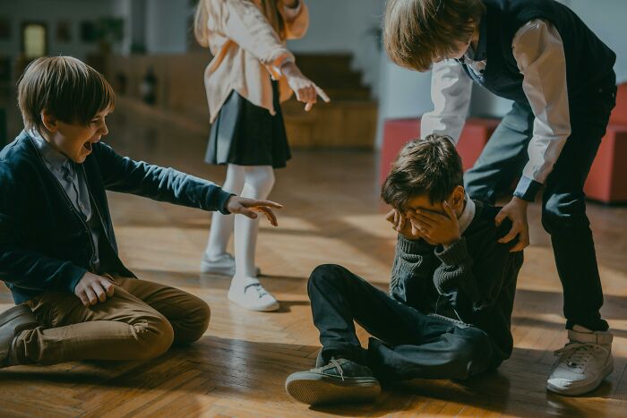 Kids interacting indoors, one sitting upset while others point and laugh, illustrating human understanding challenges.