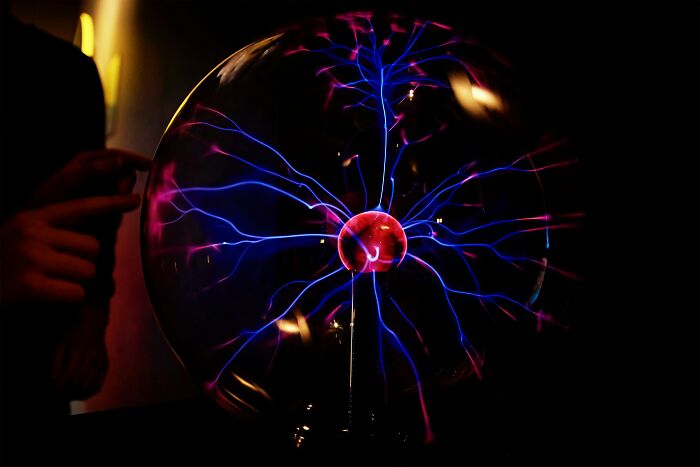 Plasma globe with pink and blue lightning-like beams; hand near glass surface.