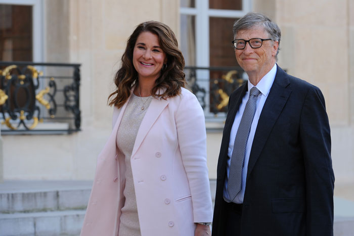 A man and woman standing outdoors, smiling, both in formal attire, related to Epstein Island discussion.