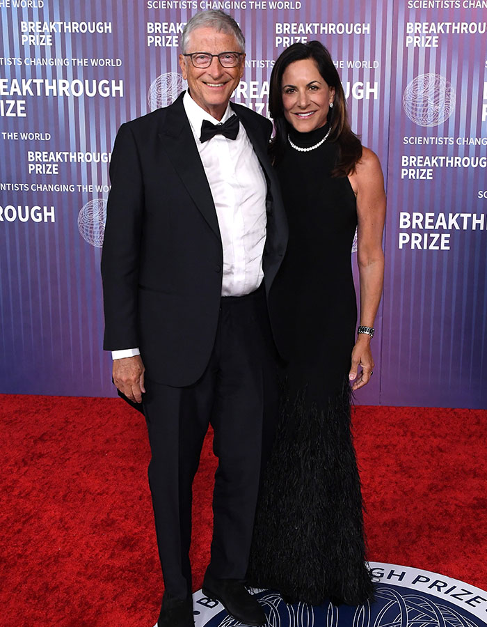 Bill Gates at a formal event on the red carpet, smiling and posing with a woman in a black gown.