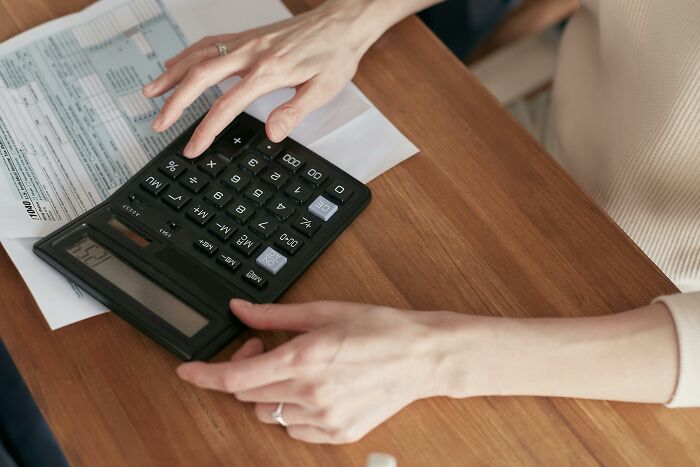 Hands using a calculator on a wooden desk, with papers, highlighting weight-loss budgeting strategies.