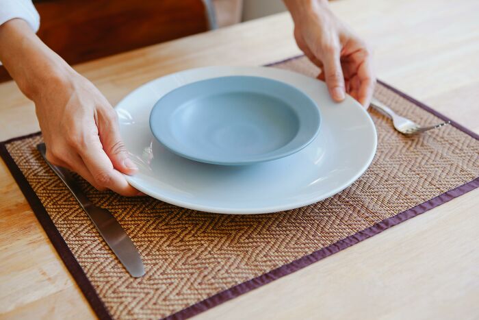 Hands placing a small bowl in a large plate on a woven mat, symbolizing food swaps for weight-loss.