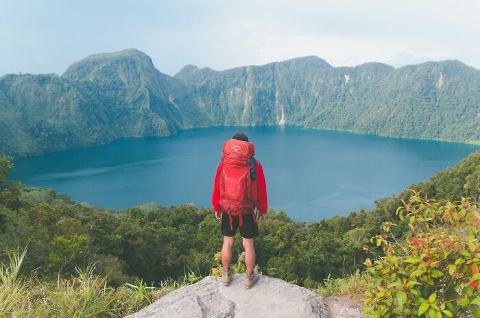 Person hiking with a red backpack overlooking a lake and mountains, exemplifying weight-loss tips like fun walks.