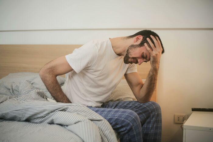 Man sitting on bed in pajamas, looking stressed; referencing weight-loss challenges and tips.