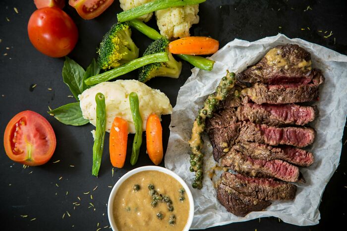 Healthy weight-loss meal with sliced steak, vegetables, and sauce on a dark background.