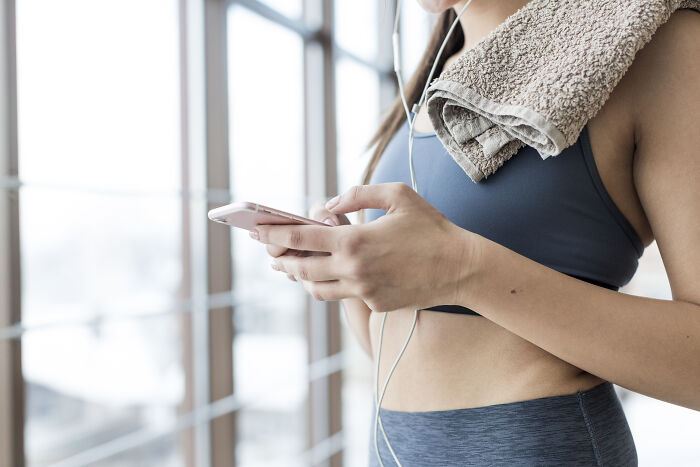 Woman in workout attire, holding a smartphone with earbuds and a towel, embracing weight-loss lifestyle.