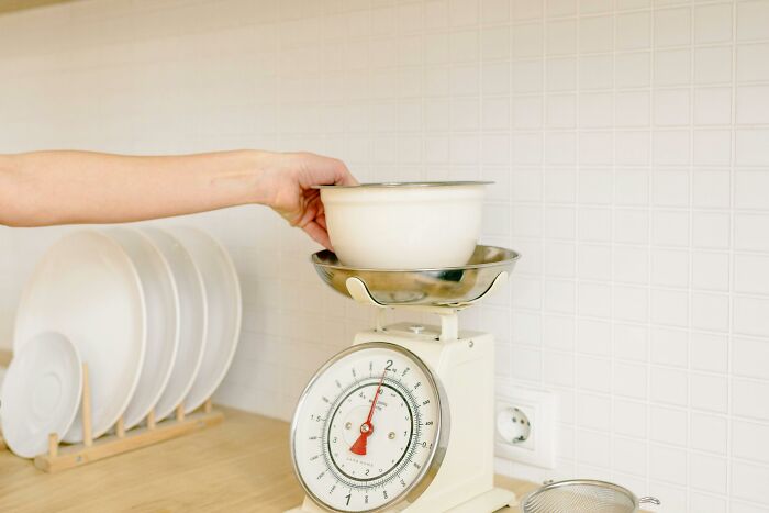 Hand placing bowl on kitchen scale for weight-loss food swaps.