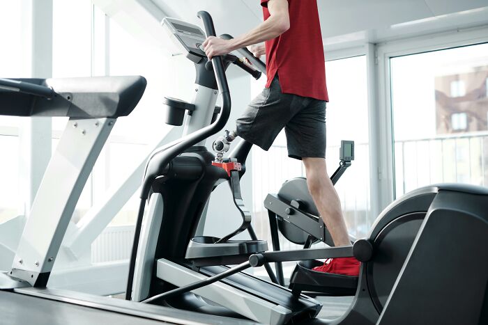 Person exercising on an elliptical machine, focusing on weight-loss fitness in a bright gym setting.