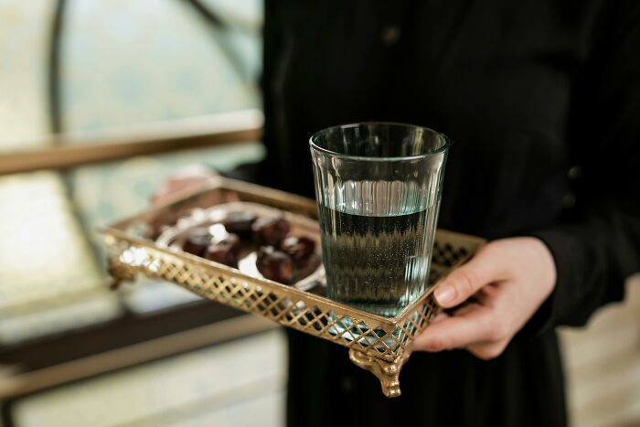 A person holds a tray with a glass of water and dates, illustrating weight-loss tips.