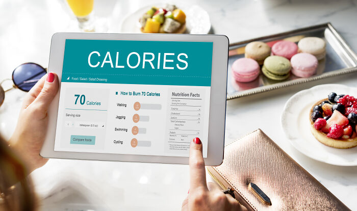 Person using a tablet with a calorie-tracking app, surrounded by desserts and a purse, focusing on weight-loss tips.