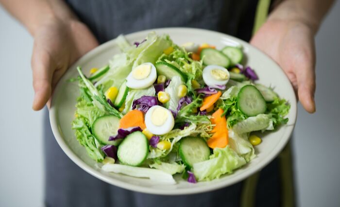 Hands holding a fresh salad with cucumbers and boiled eggs, illustrating weight-loss tips.