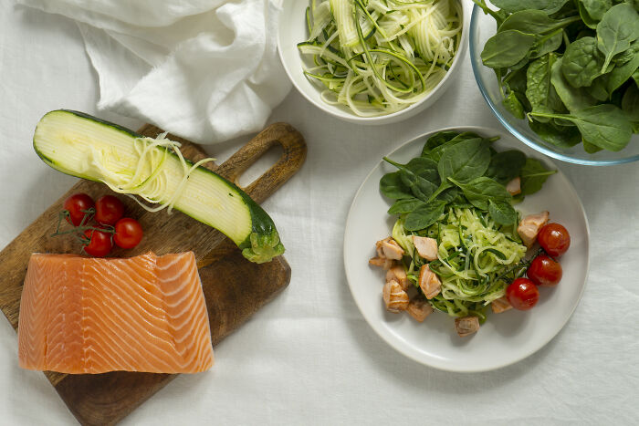 Salmon, zucchini noodles, spinach, and tomatoes on a table, showcasing food swaps for weight-loss.