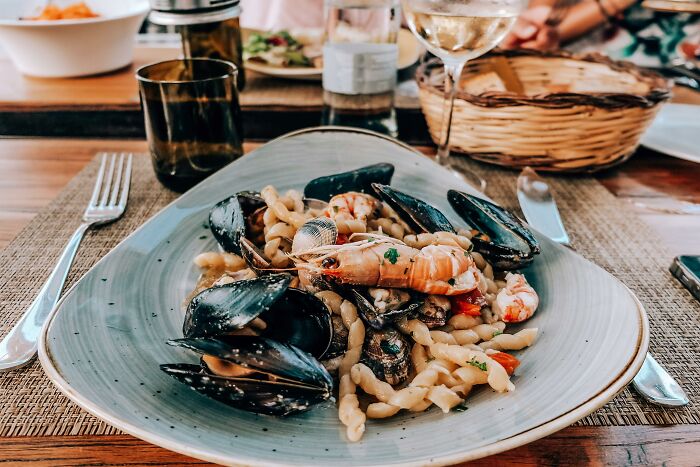 Seafood pasta dish, an example of food swaps for weight-loss, served at a wooden table with wine and bread.