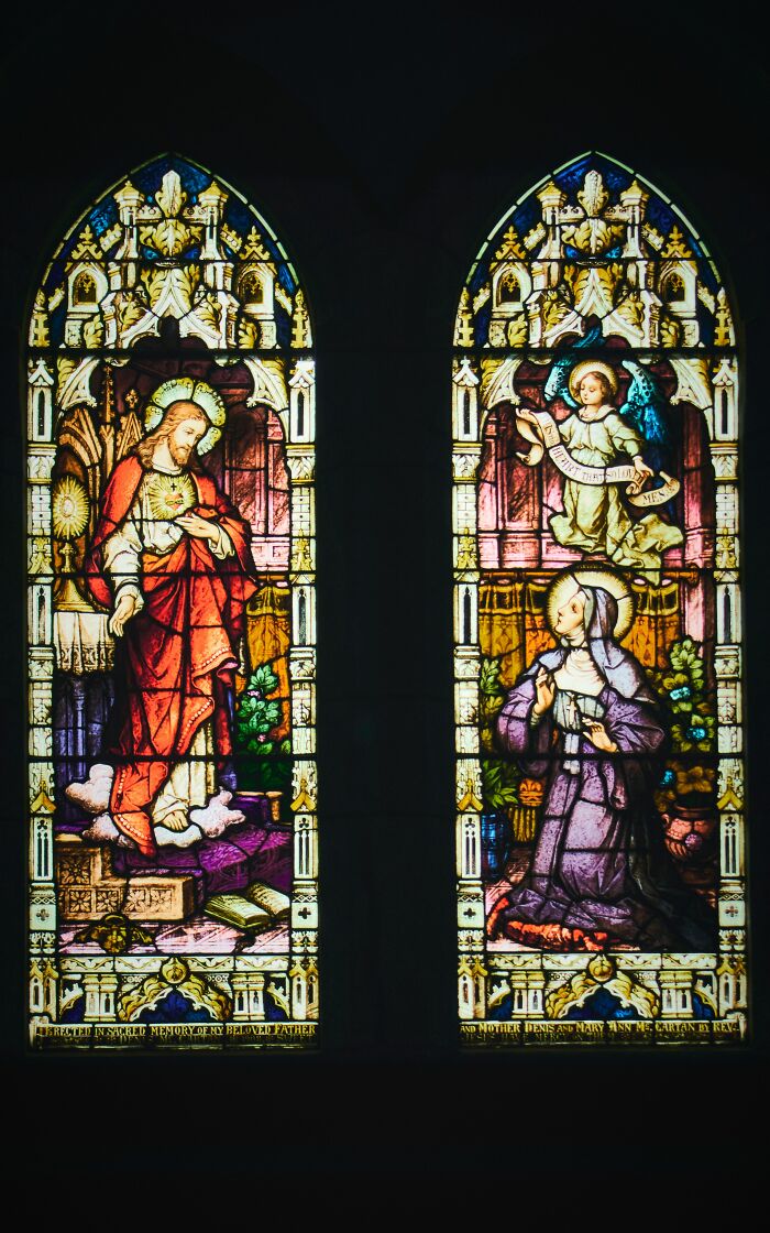 Stained glass window depicting religious figures in a church setting, with intricate designs and vivid colors.