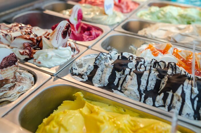 An assortment of colorful gelato flavors in metal tubs, topped with sauces, representing a lifetime supply experience.