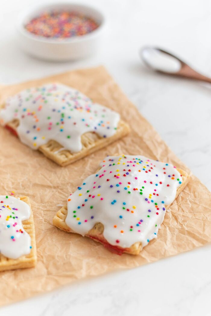 Frosted pastries with sprinkles, representing a lifetime supply, on parchment paper with a bowl of sprinkles.