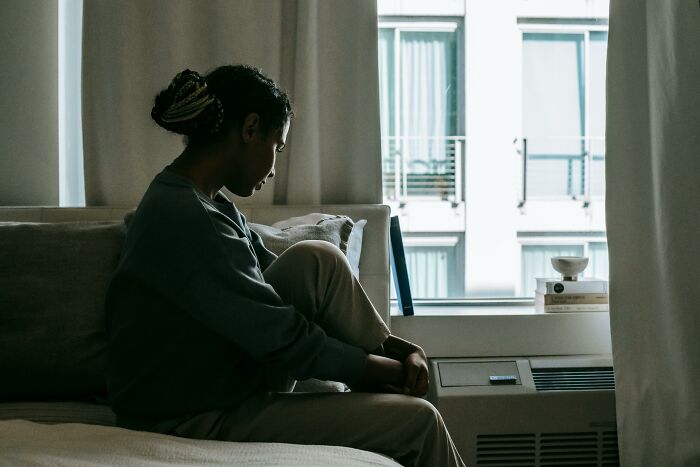 Person sitting on a bed by a window.