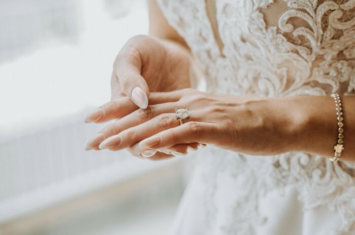 Close-up of a woman in a wedding gown admiring a diamond ring, related to the biggest scam in human history.