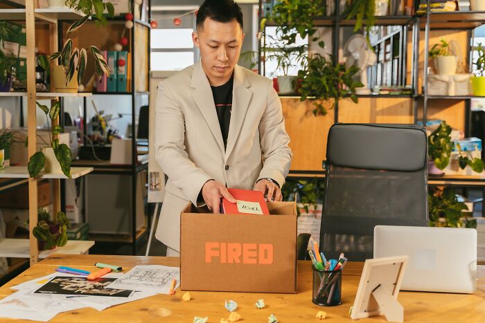 Man packing a "Fired" box in an office, representing a savage and revengeful job exit.