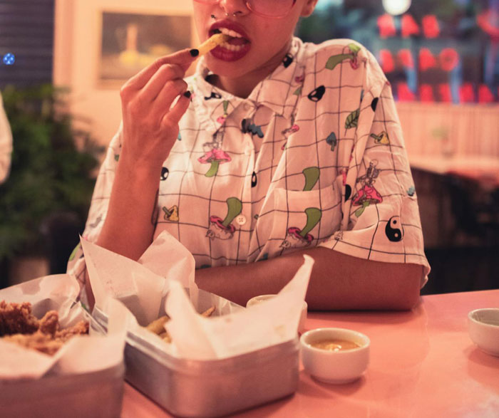 Person in a patterned shirt eating fries at a restaurant, with interesting dishes on the table.