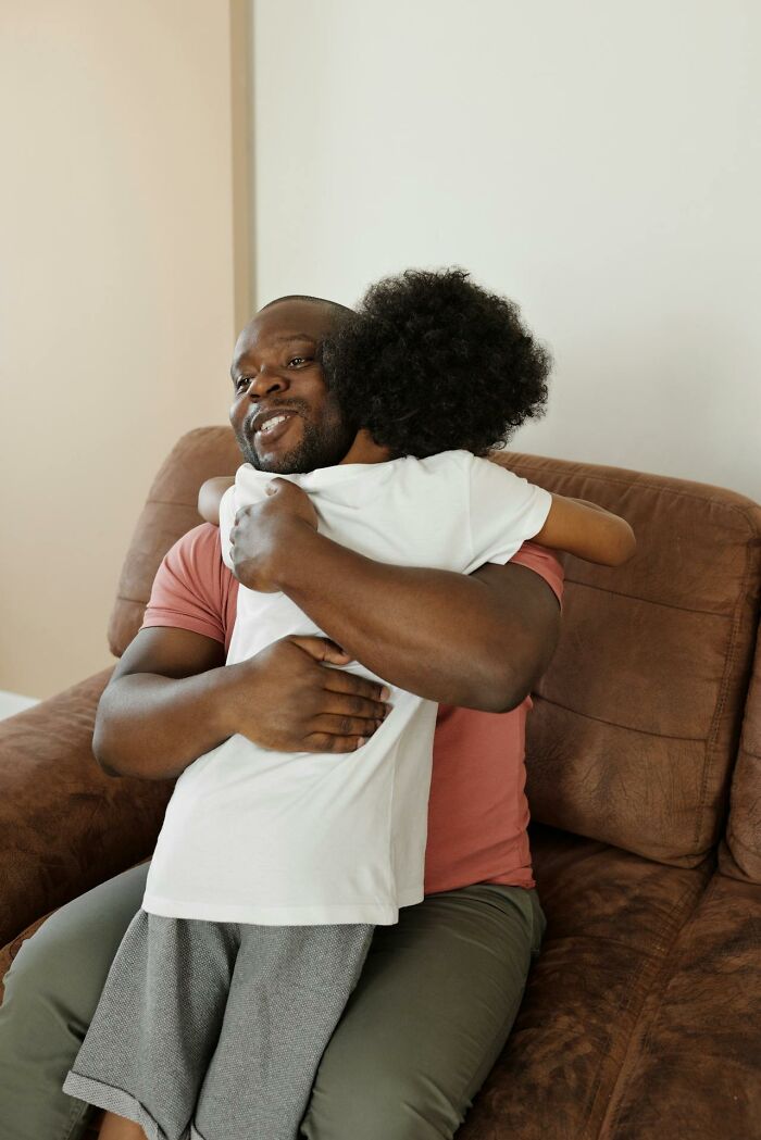 A man and child hugging on a brown sofa, embodying positive social norms and affection.