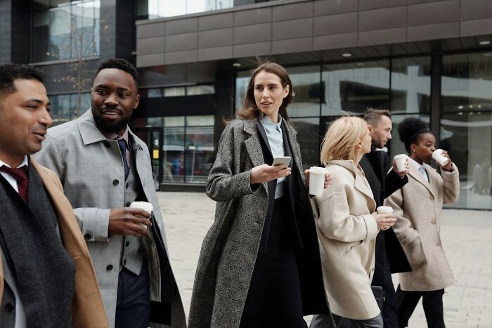 People in business attire walking and holding coffee, representing social norms.