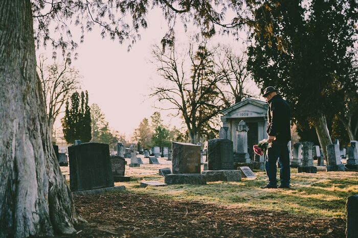 Person holding flowers in a cemetery, contemplating social norms.