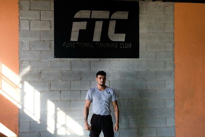 Man standing in front of FTC gym sign, wearing a gray shirt, unsettling expression.