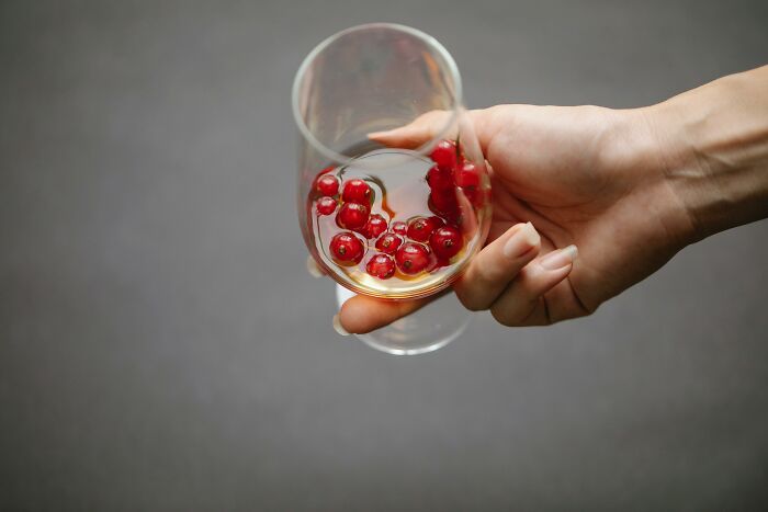 Hand holding a wine glass with red berries.