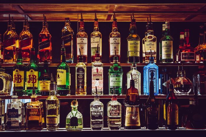 Bottles of various liquor brands neatly arranged on shelves in a dimly lit bar setting.