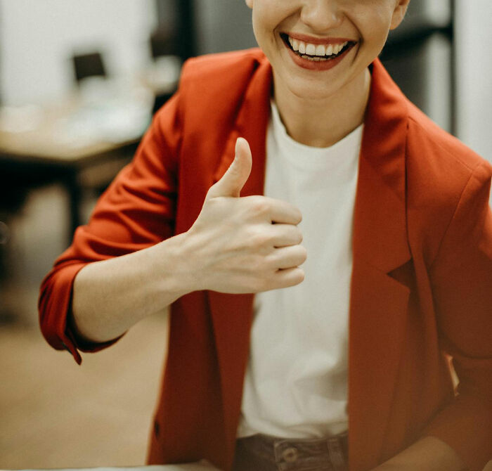 Person in a red blazer giving a thumbs up, smiling confidently, embodying normalized social norms.