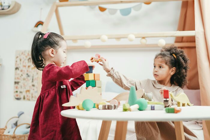 Children playing with wooden blocks at a small table, exploring creativity and teamwork in a cozy room setting.