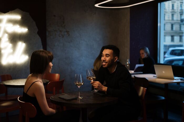 A couple enjoying wine at a dimly lit restaurant, discussing social norms.