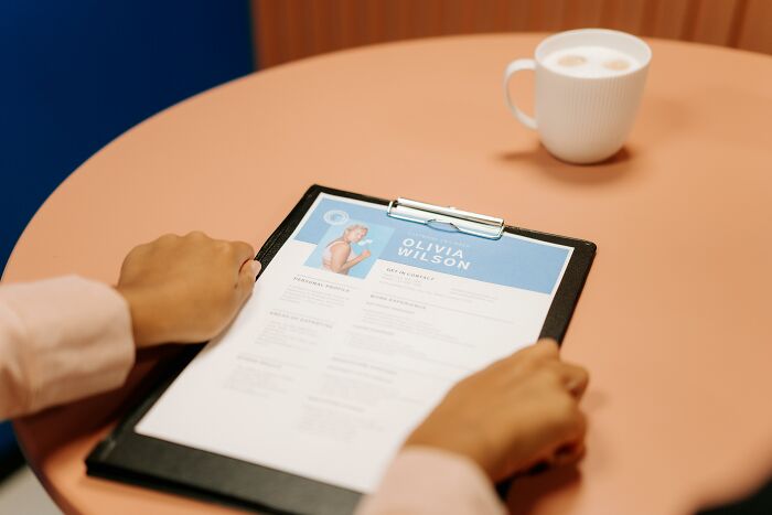 Person reviewing a resume on a clipboard with a cup of coffee nearby, focusing on potential red flags.