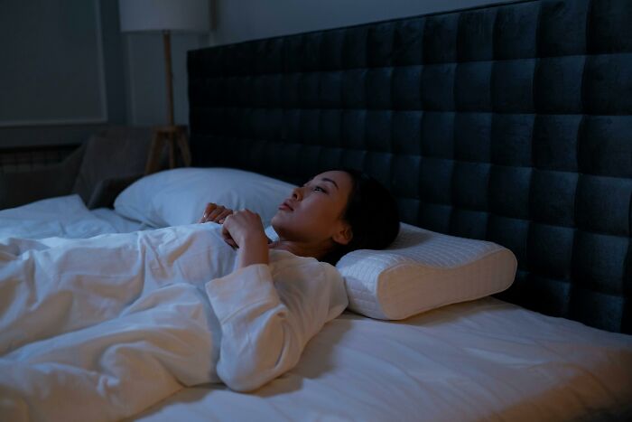 Person lying awake in bed at night, appearing thoughtful.