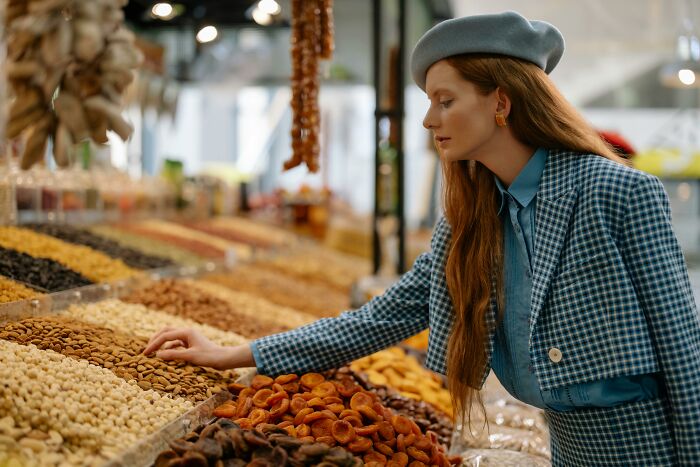 Woman in a blue outfit browsing dry fruits at a market, representing interests appeal for older adults.