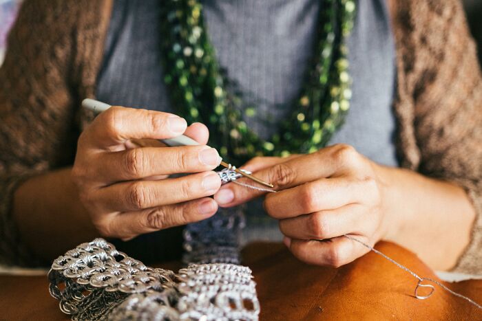 Hands crocheting with a metal hook on a wooden table.