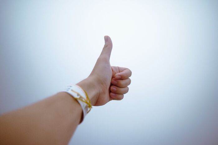 Thumbs up gesture against a plain background, symbolizing agreement with social norms.