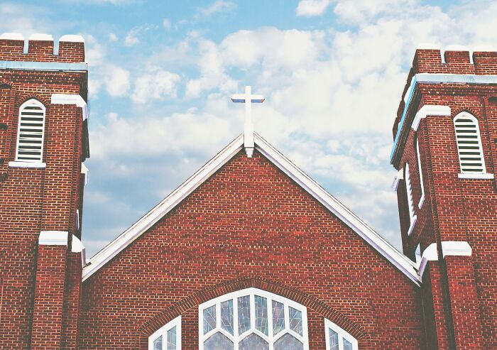 Old red brick church with twin towers under a cloudy sky.